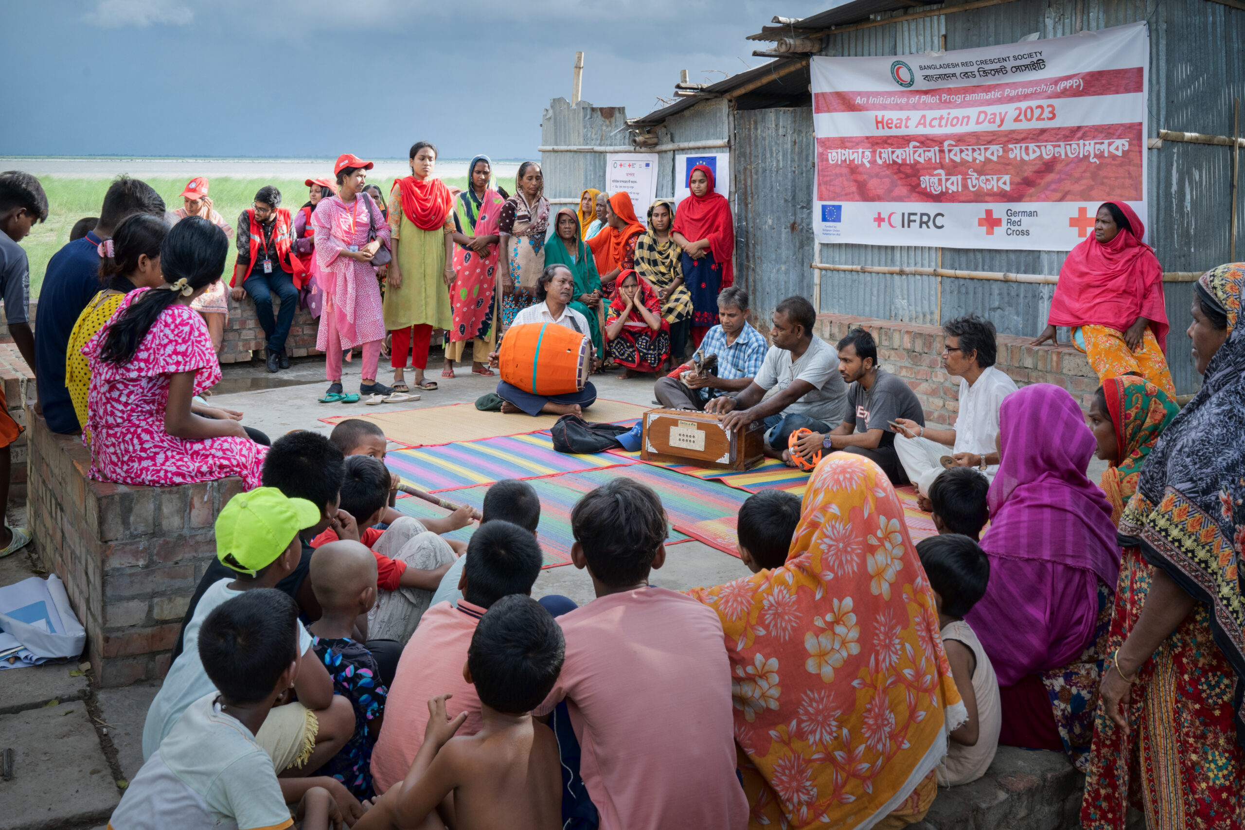 Bangladesh Red Crescent volunteers stand before a large group of slum dwellers, informing them about the dangers of heatwaves. 