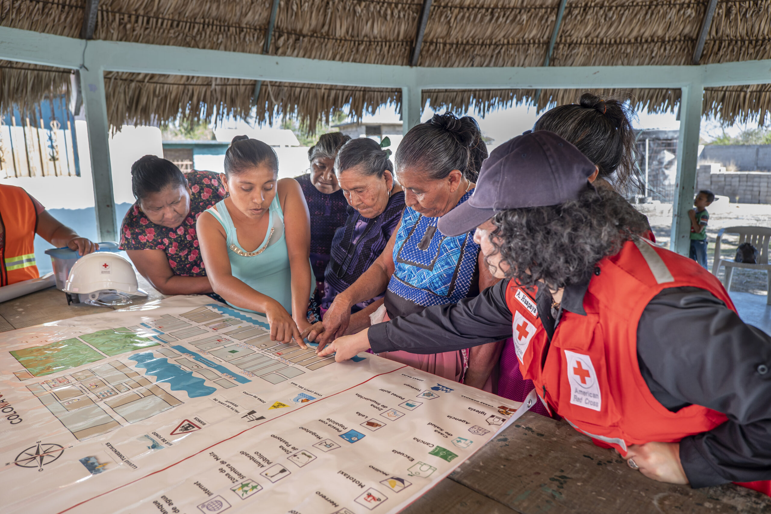 A volunteer wearing a Mexican red cross vest works with women translating the information in Ombeayuits, the local language. Four women from the community point at a risk map and learning escape routes.  