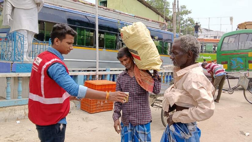 indian_rc_carry Indian Red Cross volunteer offers water to two men on the street during a heat awareness activity, with buses and other people in the background.