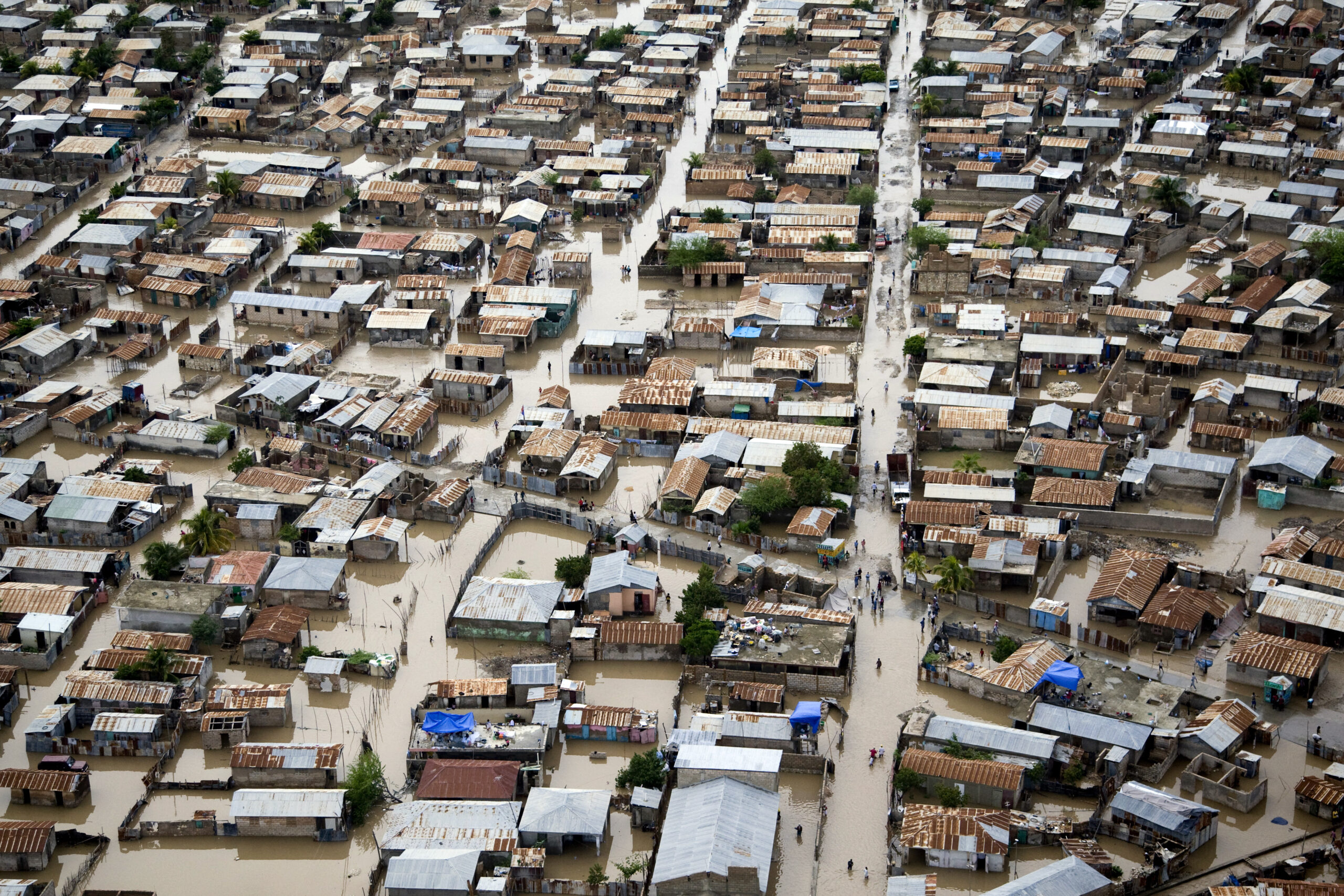 Aerial view of flooded streets and densely packed homes in Gonaives, Haiti, showing the impact of Hurricane Tomas on an unplanned urban settlement.