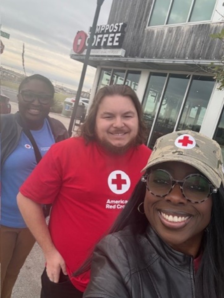 ARC Community Risk Reduction Coordinators Dr. April Masha Jones taking a selfie with Robert Nicholas Crowe and Dr. Shenika Young, all wearing Red Cross apparel, standing in front of a coffee shopp