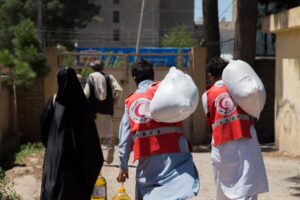 Two Afghan Red Crescent Society volunteers carry large sacks of food and cooking oil to deliver to community members during a relief distribution operation in Afghanistan.