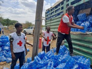 Ethiopian Red Cross volunteers in vests unload large quantities of bottled water from a truck during a relief distribution operation.