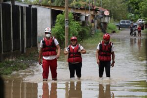 Three Guatemalan Red Cross volunteers in life jackets and helmets wade through a flooded street during a flood response operation in Guatemala.