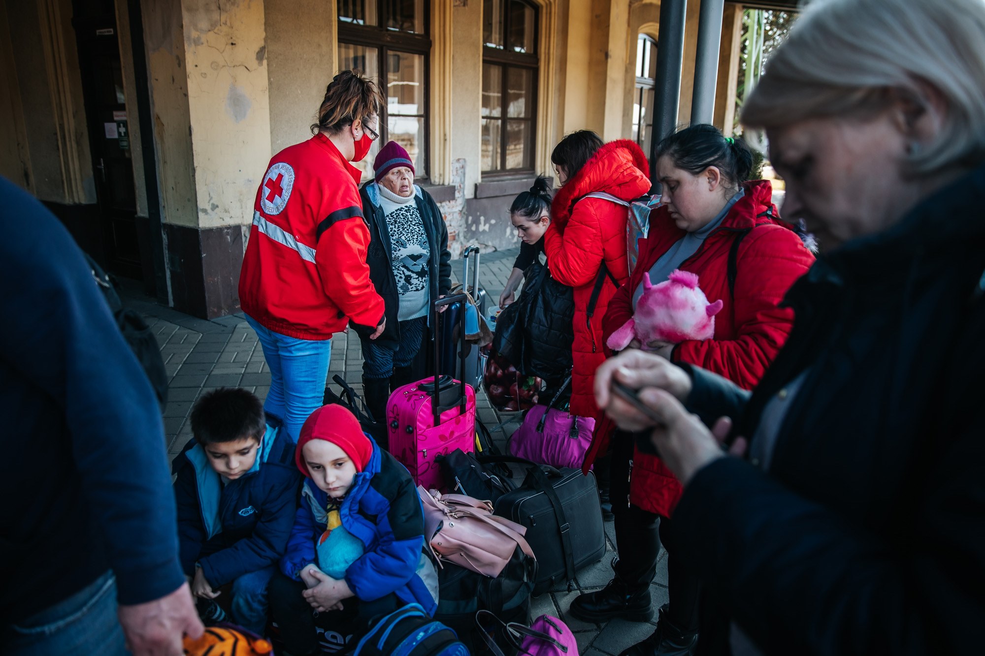 A Hungarian Red Cross volunteer assists a group of Ukrainian refugees, including women and children with luggage, at a train station on the Hungarian border.