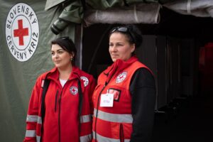Two Slovak Red Cross volunteers in uniform stand in front of a Red Cross tent at a reception point for Ukrainian refugees at the Slovak border.