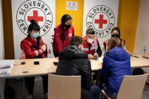 Slovak Red Cross volunteers and an IFRC cash and voucher assistance officer register and assist Ukrainian refugees at a reception desk at a Slovak Red Cross facility in Slovakia.