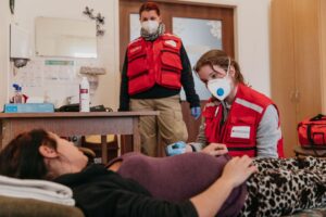 A Hungarian Red Cross emergency healthcare volunteer examines a pregnant woman lying on a bed while a colleague observes during a medical response operation in Hungary.