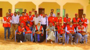 A large group of approximately 25 SRCS staff and volunteers, most wearing red vests, pose for a group photo outside the SRCS branch office building.
