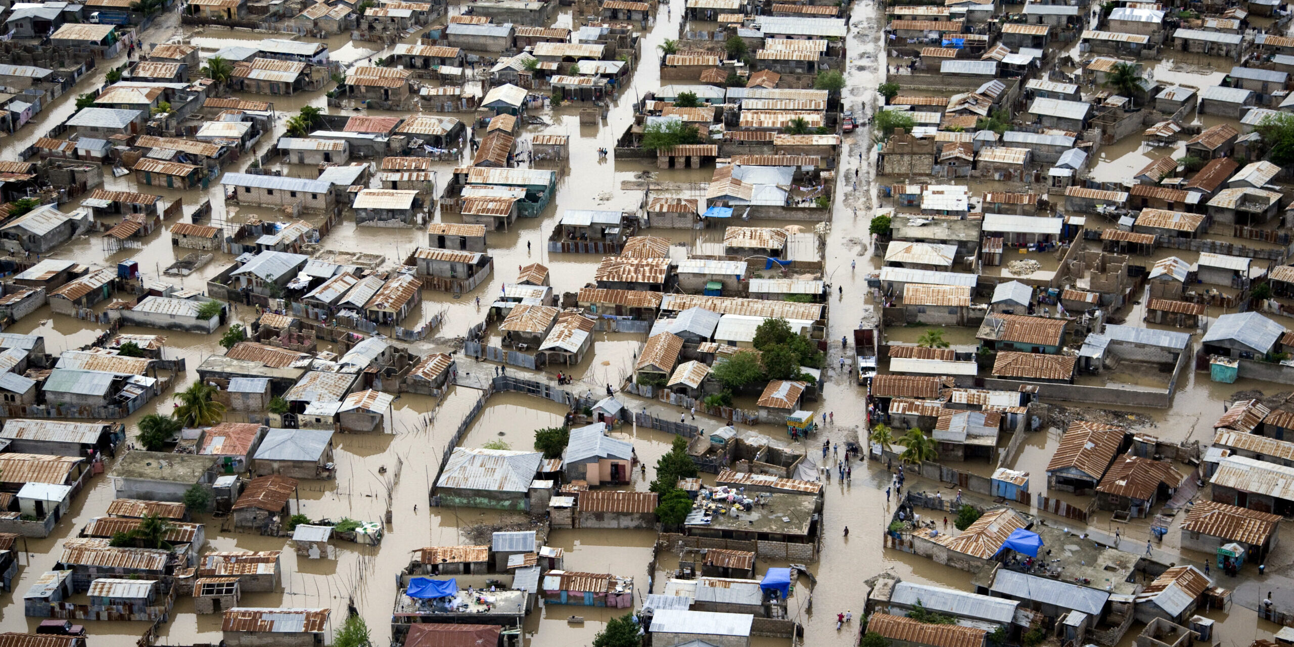 Aerial view of flooded streets and densely packed homes in Gonaives, Haiti, showing the impact of Hurricane Tomas on an unplanned urban settlement.