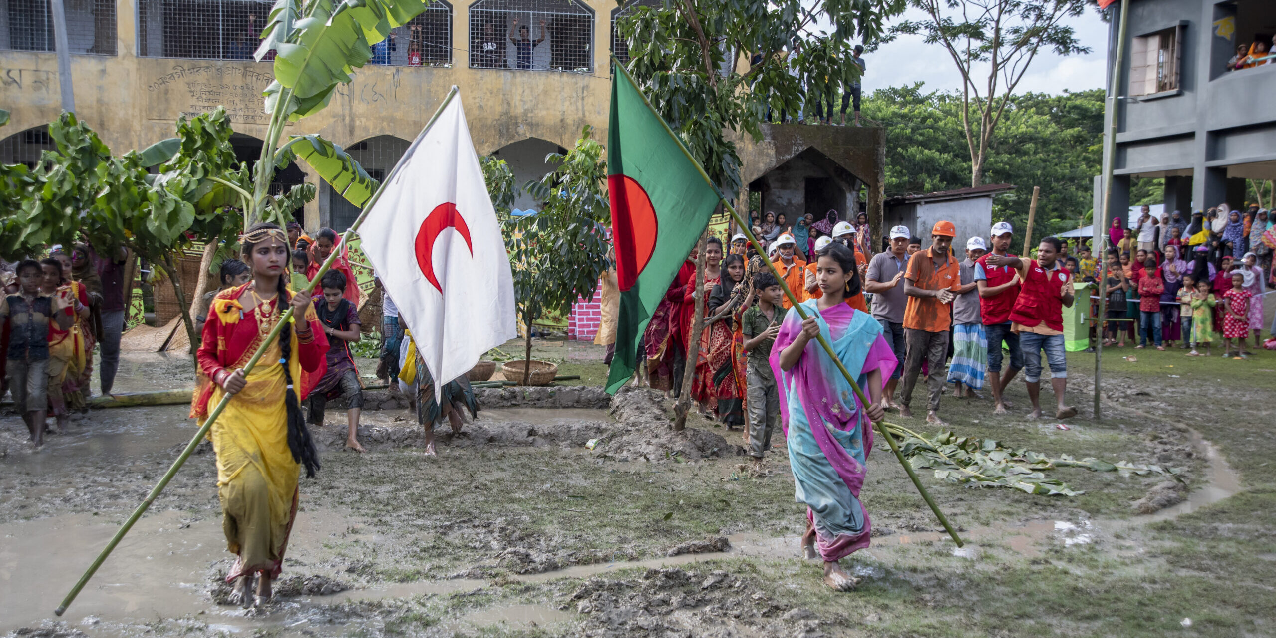 Community members in Bangladesh take part in a disaster preparedness drill, carrying the Bangladesh Red Crescent and national flags through a flooded area. The exercise highlights the role of anticipatory action and pre-financing in enabling swift early response to coastal hazards.