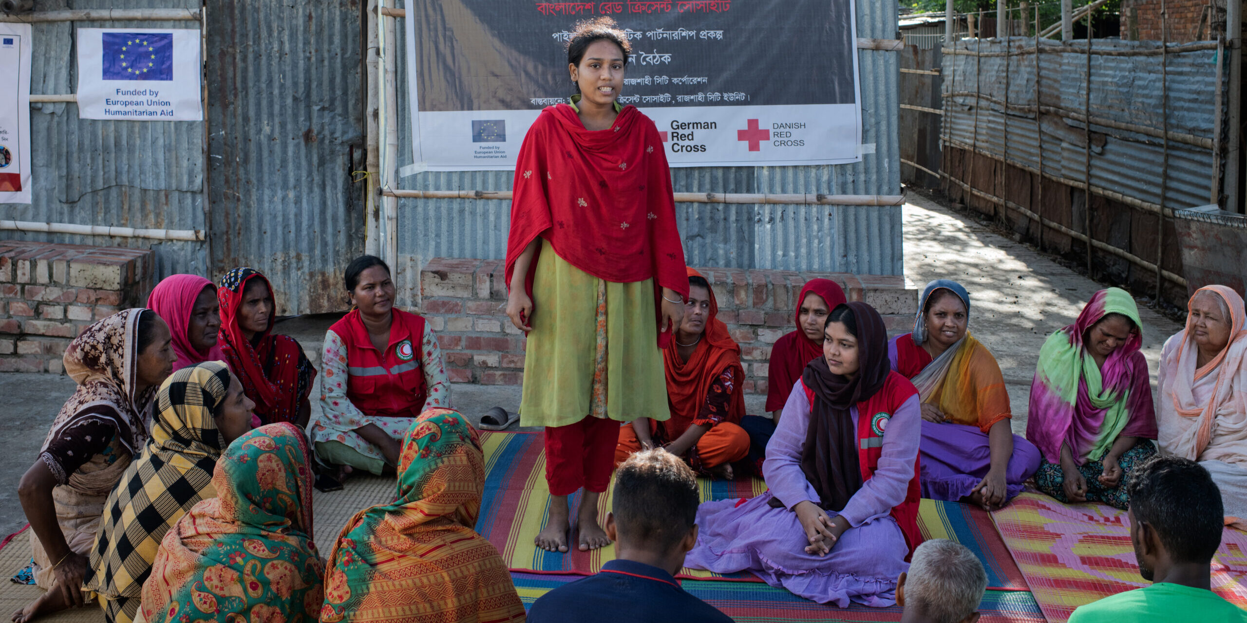 A Red Cresent volunteer standing before a group of women in Bangladesh informing how to cope with heatwaves